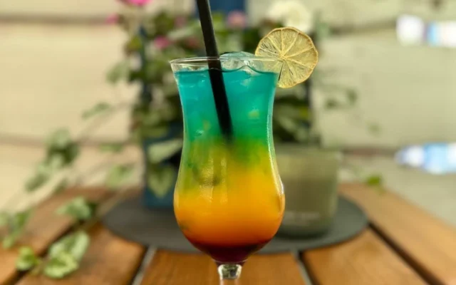 Kolorowy drink warstwowy w kieliszku z plasterkiem suszonej limonki i czarną słomką