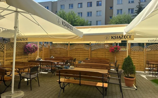 Ogródek letni pizzerii Tabia: drewniane stoły i ławy pod parasolami, wiszące kwiaty i drewniane ogrodzenie