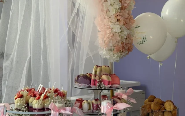 Słodki stół komunijny: makaroniki, deserki w pucharkach, orzeszki, kwiaty z hortensji i balony z napisem „Komunia Święta”
